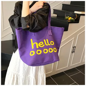 Detalle de un bolso tote de lona morada con estampado amarillo hello y correas.