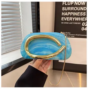 Detail shot of a blue marble texture clutch bag featuring a sleek gold curved handle