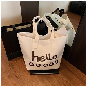 Vista detallada de un bolso shopper grande de lona blanca con estampado 'hello' café