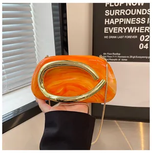 Detailed close-up of orange marbled evening clutch bag featuring a chunky gold C-handle