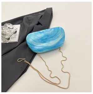 Detail view of the blue marble acrylic clutch bag with elegant gold snake chain strap.