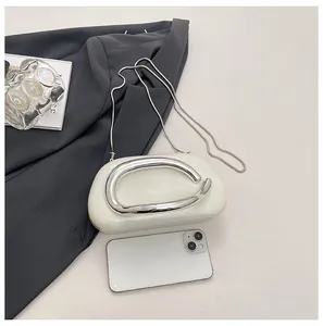Detail of white marble clutch showing metallic C-handle and size comparison with phone