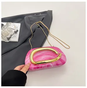 Close-up shot of a pink marbled acrylic evening clutch bag featuring an elegant gold handle