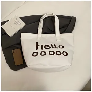 Detalle de un bolso tote de lona blanca con estampado 'hello' en un ambiente cotidiano.