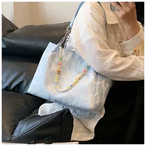 Stylish light blue tote bag with textured heart pattern and a colorful beaded chain accessory