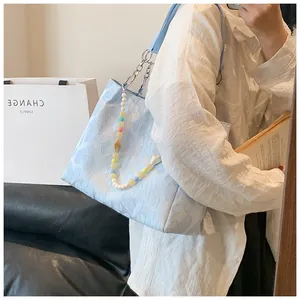 Close-up of a light blue textured tote bag with a chic colorful beaded chain accessory.