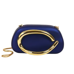 Close-up detail of a navy blue evening clutch with a bold gold C-shaped metal ornament