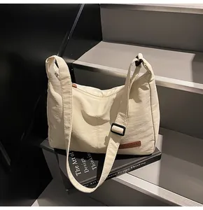 Minimalist cream white messenger bag displayed on book with adjustable strap detail