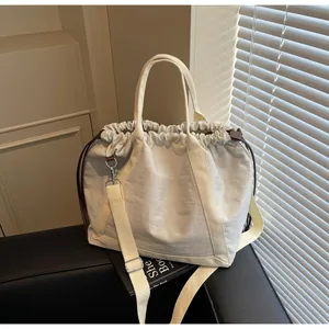 Minimalistische crème nylon crossbodytas met trekkoord op een zwart boek.