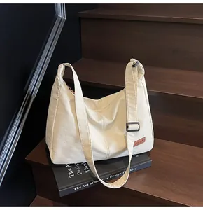 Large minimalist cream canvas hobo bag placed on a vintage book on dark wooden stairs