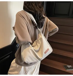 Large beige minimalist crossbody bag shown on a model in a cozy indoor setting