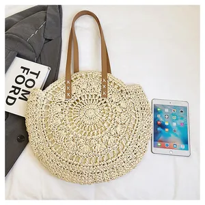 Round straw woven beach bag with floral hollow design, brown leatherette handles.