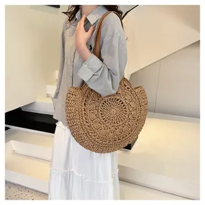 Detailed view of a round hand-woven straw shoulder bag with hollow floral pattern on a model.