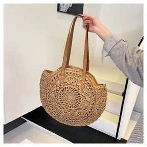 Handheld view of a round straw beach bag featuring intricate hollow floral woven patterns