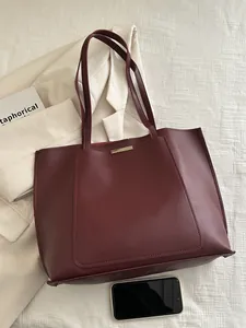 Détail d'un grand sac cabas bordeaux en cuir souple posé sur un blazer blanc neutre