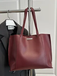 Détail d'un sac cabas en cuir bordeaux suspendu à un portant de vêtements professionnel
