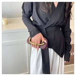 Detail view of a luxury burgundy evening clutch bag with a unique gold metal handle.