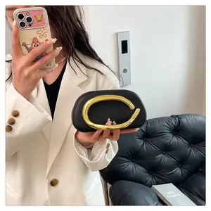 Close-up of minimalist black evening clutch with elegant gold C-shaped handle.