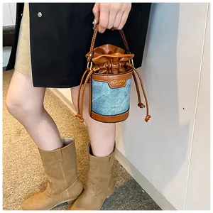 Close-up of a denim and leather patchwork drawstring bucket bag held by a model.