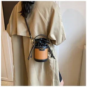 Minimalist color-block drawstring bucket bag shown as crossbody on trench coat
