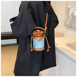 Detail of denim and leather cylindrical bucket bag with drawstring and golden brand logo