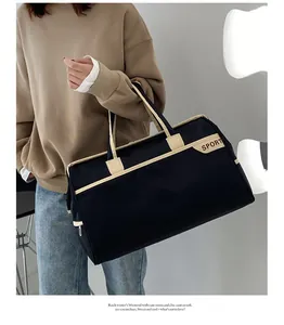 Model hält eine große schwarz-beige wasserdichte Reisetasche in einem Studio-Setting