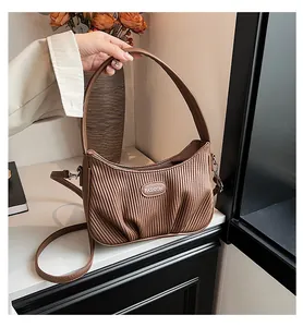 Detailed view of a brown pleated cloud handbag held by hand with a floral background.