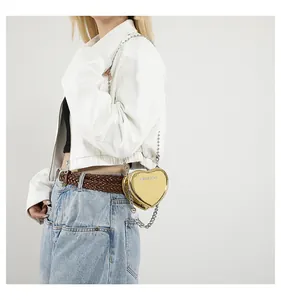 Detail of heart-shaped gold metallic crossbody bag worn with white jacket and jeans