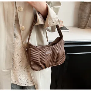 Detail view of a brown pleated cloud handbag carried by a model in a trench coat