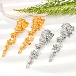 Close-up detail of elegant gold and silver metal floral drop earrings on a white stand