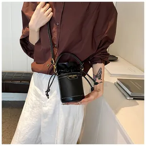 Detail of the black cylinder bucket bag with drawstring closure and gold logo branding.