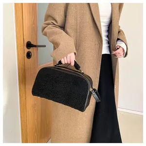 Detail view of a black furry large capacity cosmetic handbag held by a fashion model