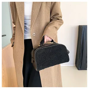 Detail view of black textured sherpa cosmetic handbag held by model in brown coat