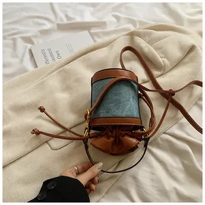 Close-up view of a stylish denim and leather patchwork cylinder bucket bag with drawstring.