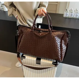 Close-up detail of a dark brown woven leather travel bag placed on a white suitcase