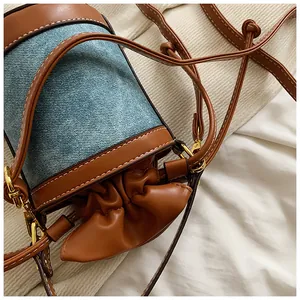 Detail of denim and brown leather patchwork cylindrical bucket bag with drawstring