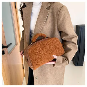 Detailed view of a brown fuzzy sherpa cosmetic bag held by a model wearing a wool coat