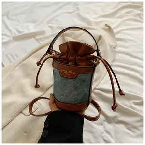 Detailed view of a spliced denim and brown leather bucket bag with a drawstring