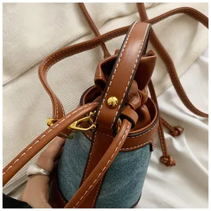 Detail view of denim and brown leather bucket bag with white stitching and drawstring
