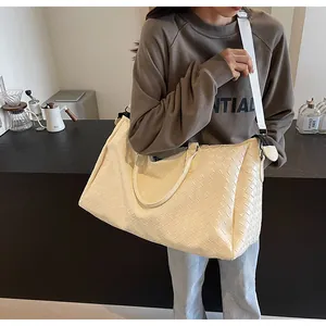 Large cream woven travel tote bag for women worn by a model in a minimalist cafe setting