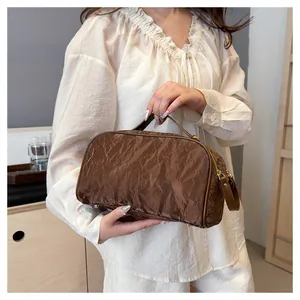 Close-up of a brown crinkled textured cosmetic bag held by a woman in light attire.
