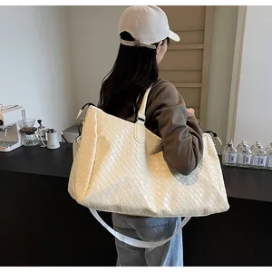 Cream woven oversized travel tote bag carried by a model in a modern cafe setting
