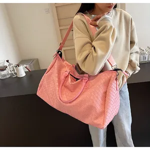Detailed view of women's pink woven travel duffel bag carried by a model on shoulder