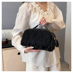 Model holding textured black cosmetic bag with gold zippers and top handle detail