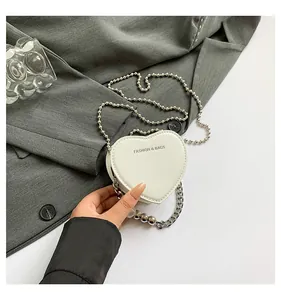 Detail view of white heart-shaped mini crossbody bag with pearl chain and silver metal strap