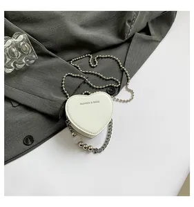 Close-up detail of white heart-shaped mini bag with stylish silver ball chains and beads.