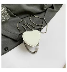 Macro detail of white heart mini bag with beaded handle and silver ball chain strap.