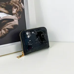 Détail d'un portefeuille noir en cuir verni avec motif crâne embossé et zip doré.