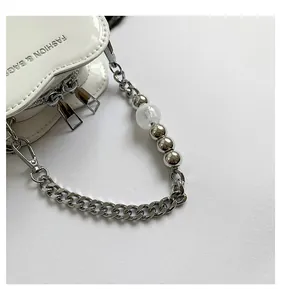 Close-up detail of a white heart-shaped mini handbag with silver beaded chain strap