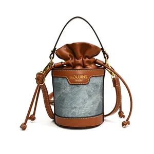A close-up view of a cylindrical bucket bag featuring denim and brown leather patchwork.